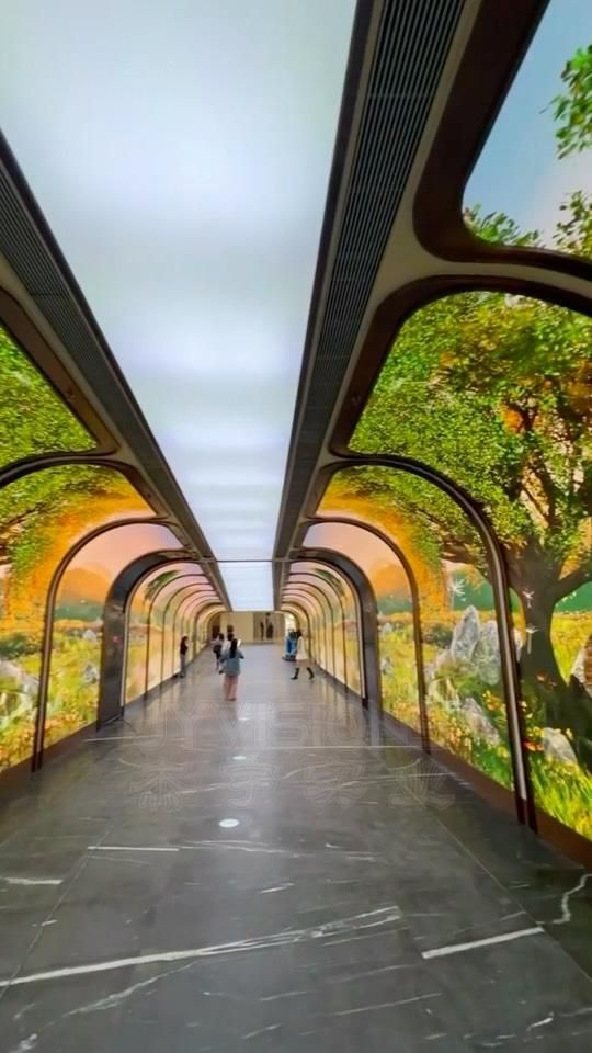 JYVISIONS curved-arch LED tunnel installation: long passageway with arched LED walls displaying a sunlit forest and meadow scene, visitors walking through