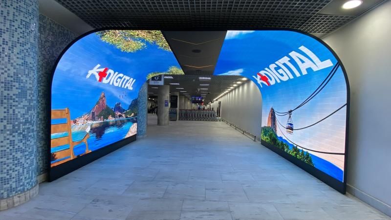 K-Digital airport LED tunnel arch displaying Rio de Janeiro scenery (Sugarloaf, Sao Conrado beach, cable car) on curved LED panels at an arrival corridor
